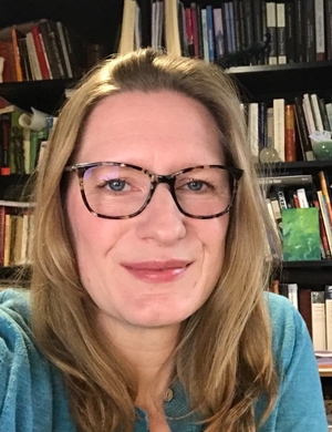 A photo of Amanda Wrigley, in front of a shelf of books. 