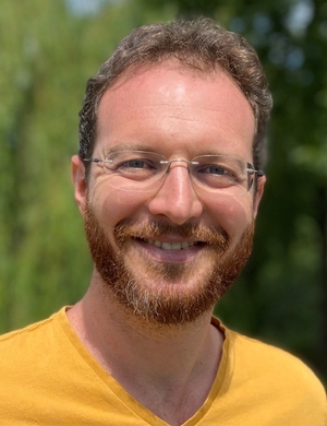 A headshot of Micha Lazarus standing outside, smiling. 