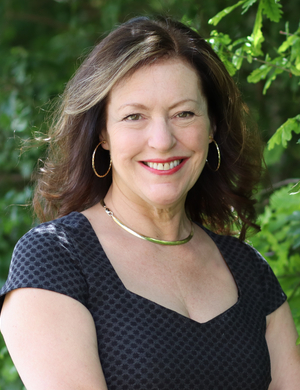 Image of Edith Hall, smiling, standing in front of a leafy background.