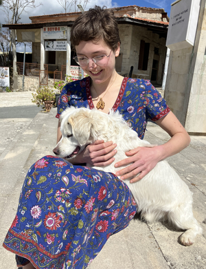 A photo of Milly Cox sitting and petting a dog in front of a Greek textile museum. 