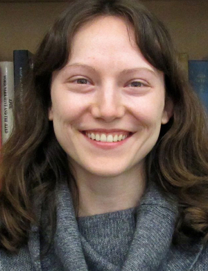 A photo of Naomi Setchell before a shelf of books, smiling.