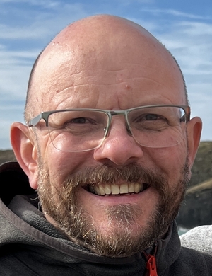 A headshot of Struan Leslie, standing outdoors and smiling. 