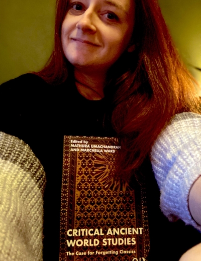 A self-portrait of Chella Ward, holding a copy of her edited volume, Critical Ancient World Studies. 