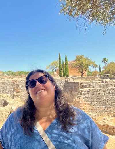 A photo of Sofia Frade standing in front of some classical ruins in the sunshine, smiling.