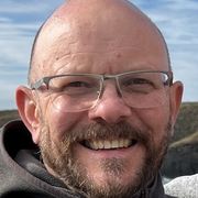 A headshot of Struan Leslie, standing outdoors and smiling. 