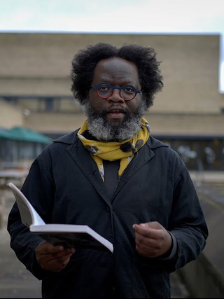 A colour photograph of Zimbabwean writer and academic, Tinashe Mushakavanhu, holding an open book