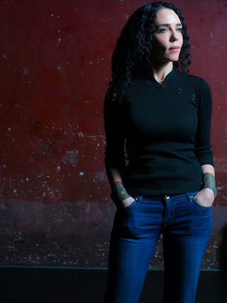 Portrait photograph of Yaël Farber stood in front of a dark red wall