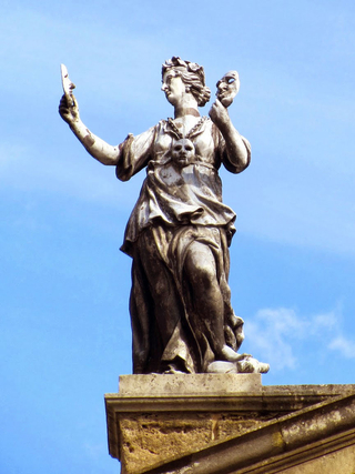 Photograph of a statue of a Muse, holding masks, with a blue sky behind