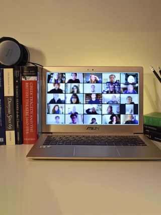 Photograph of a laptop displaying a full screen of Zoom participants (blurred faces)