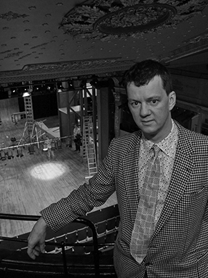 Black and White photograph of Tom Morris with the stage of the Bristol Old Vic behind and below him